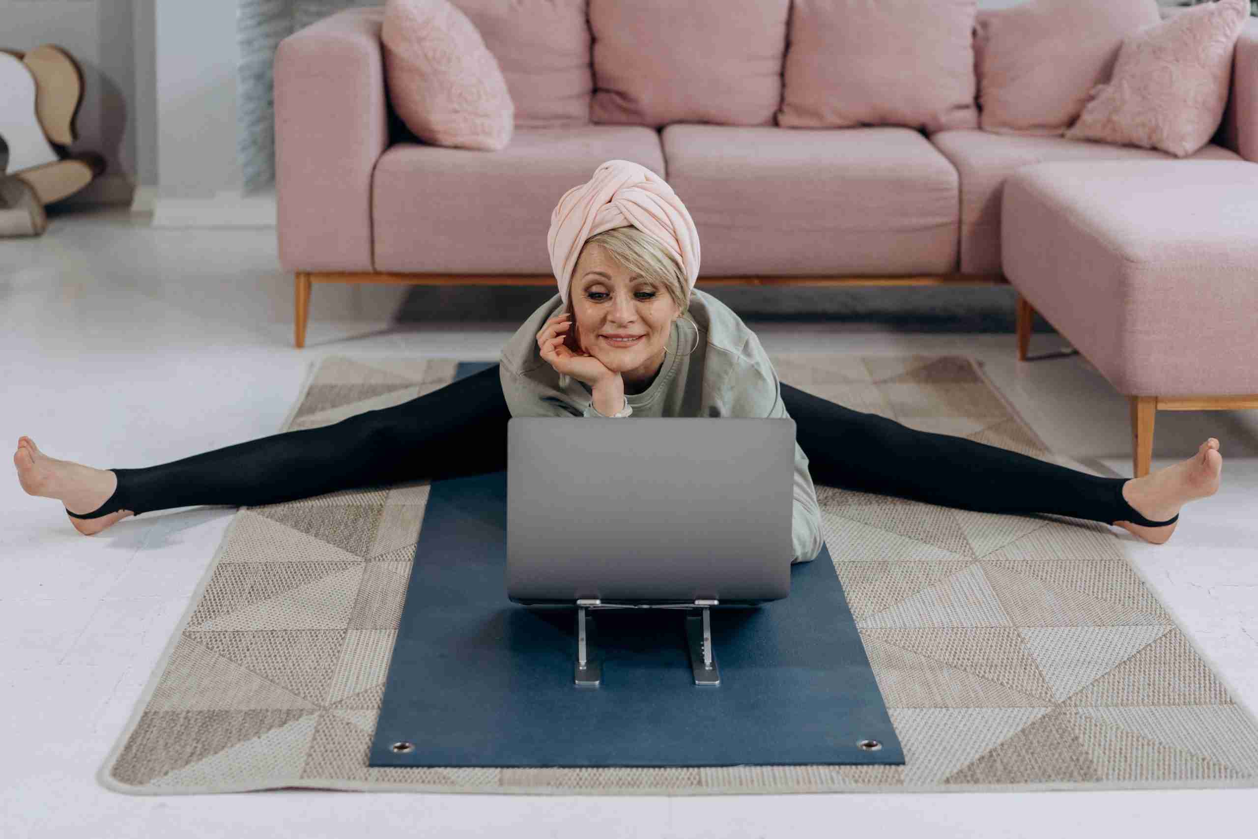 ältere Dame, die sich vor einem Laptop auf einem Teppich dehnt; Sport ist in jedem Alter gut health wellnes before-night-falls.com blog
