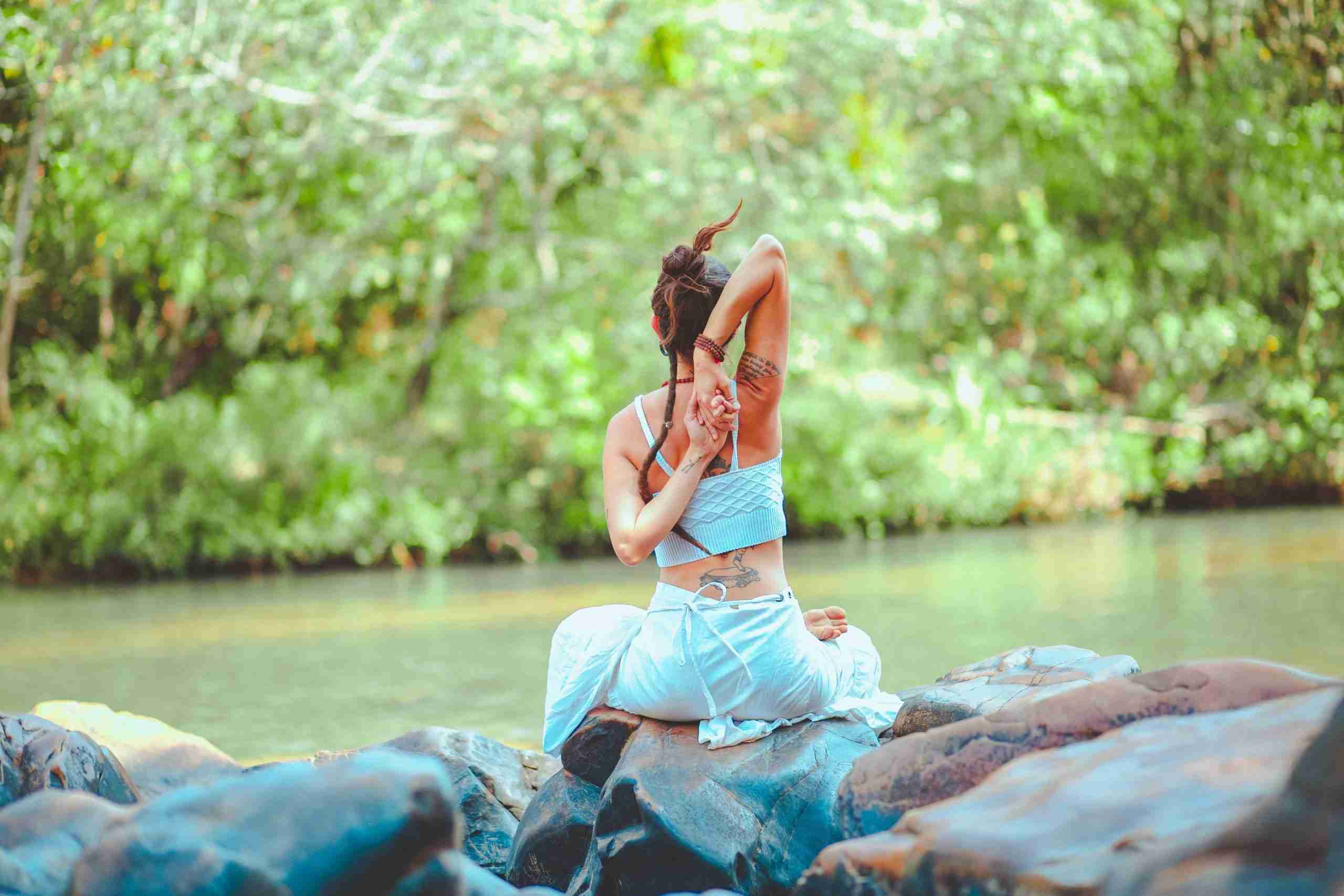 chica sentada en las rocas junto al río, estirando asuntos de estilo de vida de medicina natural antes-noche-cae.com
