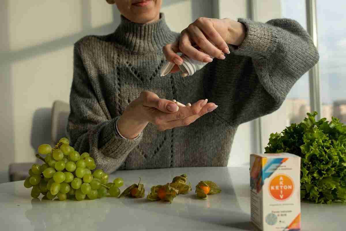 mujer mayor con pastillas de keton aktiv en la mano sentada junto a la mesa. uvas, lechuga y caja de keton aktiv en la mesa.